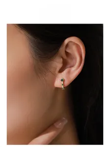 Close-up of model wearing gold hoop earrings with green zircon and white crystals