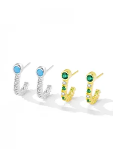 Detail of J-shaped S925 silver earrings with turquoise and emerald stones in gold and silver