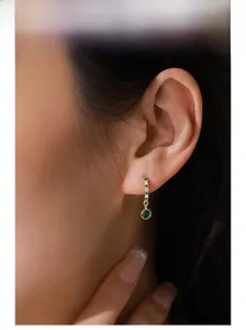 Detail of S925 silver emerald zircon drop earrings worn on ear in 14K gold finish