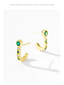 Macro detail of J-shaped gold earrings set with green emeralds and white crystals