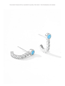 Macro detail of C-shaped S925 silver earrings with green zircon and pavé crystals