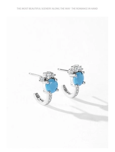 Close-up of C-shaped silver earrings with turquoise stones and shimmering zircon details