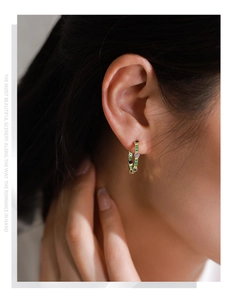 Close-up of elegant gold hoop earrings with green and purple zircon worn by a model