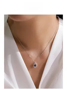Detail of sunflower pendant necklace with oval blue sapphire and white zircons on a model