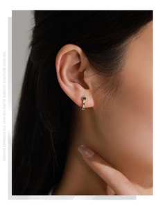 Détail de boucles d'oreilles vintage dorées en J avec des incrustations d'émeraude