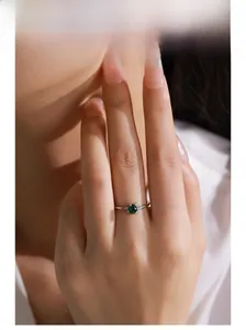 Close-up of S925 silver ring with emerald green zircon and side stone accents on finger