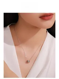 Detailed view of a silver cylinder pendant on a delicate chain worn by a female model