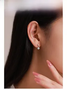 Close-up of minimalist silver flower earrings with white zircon on female ear lobe