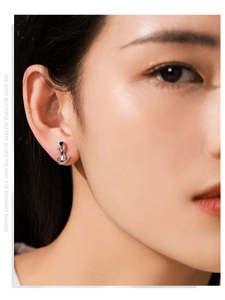 Close-up of a silver cat stud earring with a blue gemstone on a model's ear