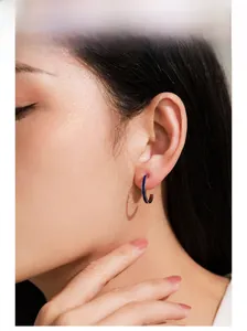 Gros plan d'un modèle portant des boucles d'oreilles C en argent 925 et émail bleu