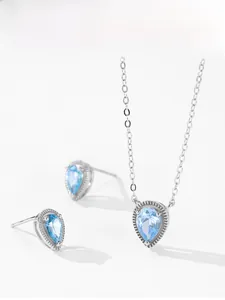 Detailopname van zilveren druppeloorbellen en ketting met lichtblauwe zirkonia steen