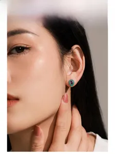 Detail of drop-shaped silver stud earring with purple crystal and green enamel finish