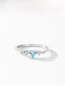 Macro view of blue heart-cut gemstone ring with white zircon accents on silver band