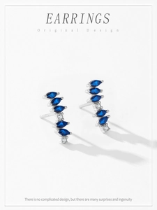 Macro shot of silver curved earrings with blue marquise zircon and white stones