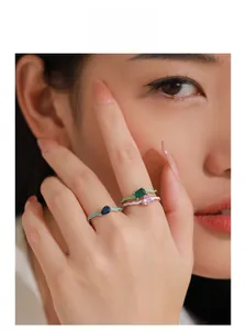 Close-up of three wavy 925 silver rings with colorful enamel and inlaid gemstones on finger
