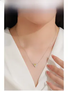 Macro detail of a silver necklace featuring a gold triangle pendant with yellow zircon