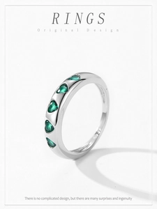 Macro view of silver ring featuring five heart-shaped emerald green zircons on white backdrop