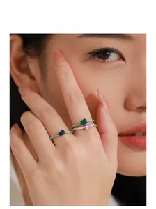 Detail of three wavy enamel rings with colorful gemstones worn by a model in a close-up shot
