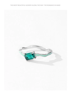 Detailed macro of wavy silver ring featuring emerald gemstone and green enamel accents