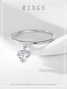 Macro detail of 925 silver ring with a sparkling heart pendant on white silk fabric