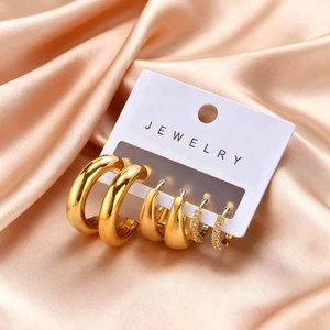 Three pairs of golden stainless steel hoop earrings set with zirconia on champagne silk