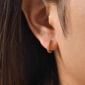 Minimalist gold-plated huggie hoop earrings with sparkling cubic zirconia on a model's ear