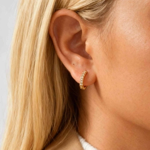 Detailed close-up of a golden huggie hoop earring with clear cubic zirconia on the ear