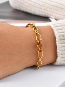 Détail d'un bracelet en maille dorée et résine ambrée porté sur un pull blanc doux