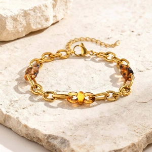 Détail d'un bracelet à maillons dorés avec perles en résine ambrée sur une surface en pierre