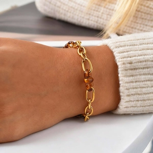 Bracelet à maillons dorés et résine ambre porté sur un pull en tricot blanc doux