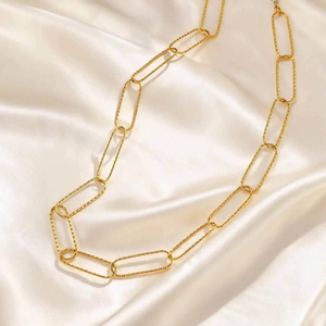 Detailed close-up of golden paperclip link chain with textured edges on silk fabric