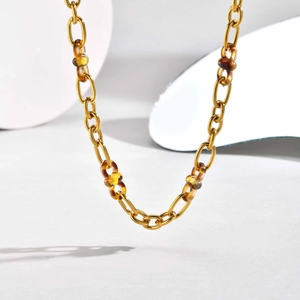 Détail d'un collier à maillons dorés avec anneaux en résine ambrée sur fond blanc pur