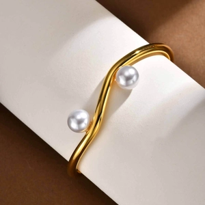Macro detail of wave-shaped golden stainless steel bracelet with glossy white pearls