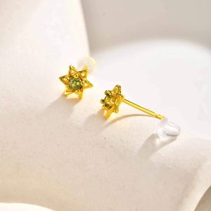Vue macro de puces d'oreilles étoile dorées avec zircon vert et fermoir silicone