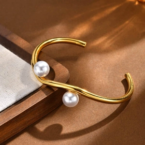 Detail of gold-plated wavy double-layer bangle with two white pearls on a warm surface
