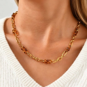 Détail du collier en chaîne dorée avec anneaux en résine ambre sur un pull blanc