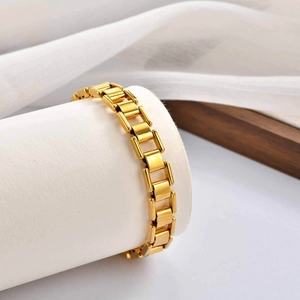 Polished gold rectangular link bracelet displayed on white stand with silk background