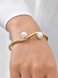 Detail of gold wavy double-layer bangle with pearls worn on wrist over white shirt