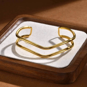 Detail view of gold wave double-layer stainless steel bangle on a wooden tray