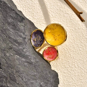 Gold geometric ring featuring colorful enamel discs set against artistic stone background