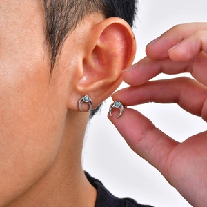 Detail of moon-shaped men's stud earring with turquoise inlay worn on ear and held by hand