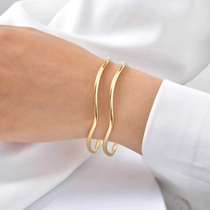 Detail of double-layer wave gold bangles with polished finish on model wrist