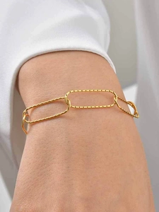 Detailed view of textured gold oval link bracelet worn on wrist with white cuff