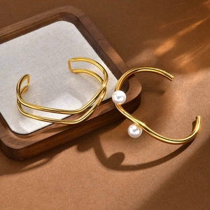 Detail of wavy gold bangle with pearls and minimalist double-layered stainless steel cuff