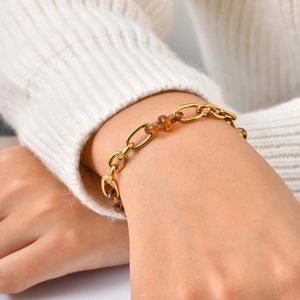 Bracelet à maillons dorés polis et résine ambrée porté sur une manche en maille