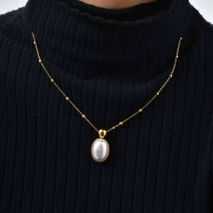 Detail of a layered golden necklace with small beads and an oval pearl on a black fabric
