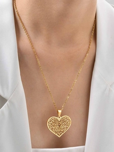 Detail of a hollow gold heart filigree pendant necklace worn by a model in white