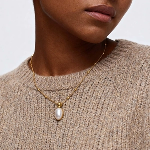 Macro shot of gold-plated double-layer chain necklace featuring oval pearl and heart charms
