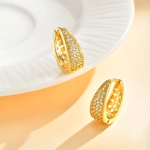 Détail de boucles d'oreilles créoles dorées en U avec micro-pavé de zircons et motifs ajourés