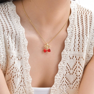 Gros plan du collier cerise avec pierres cœur rouges et nœud doré sur le décolleté